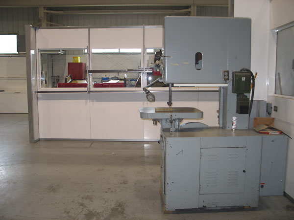 Foreground: metal cutting band saw. Background: composites fabrication area.